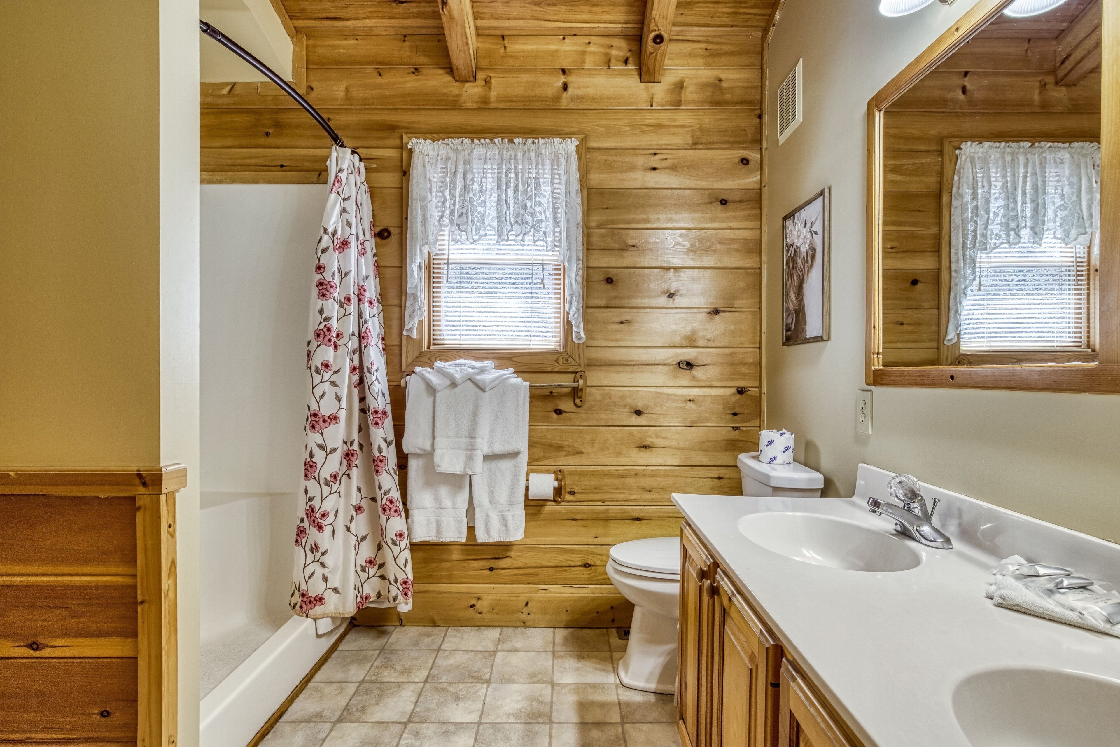 A wooden-paneled bathroom with a white sink, two towel racks, a toilet, and a shower curtain.
