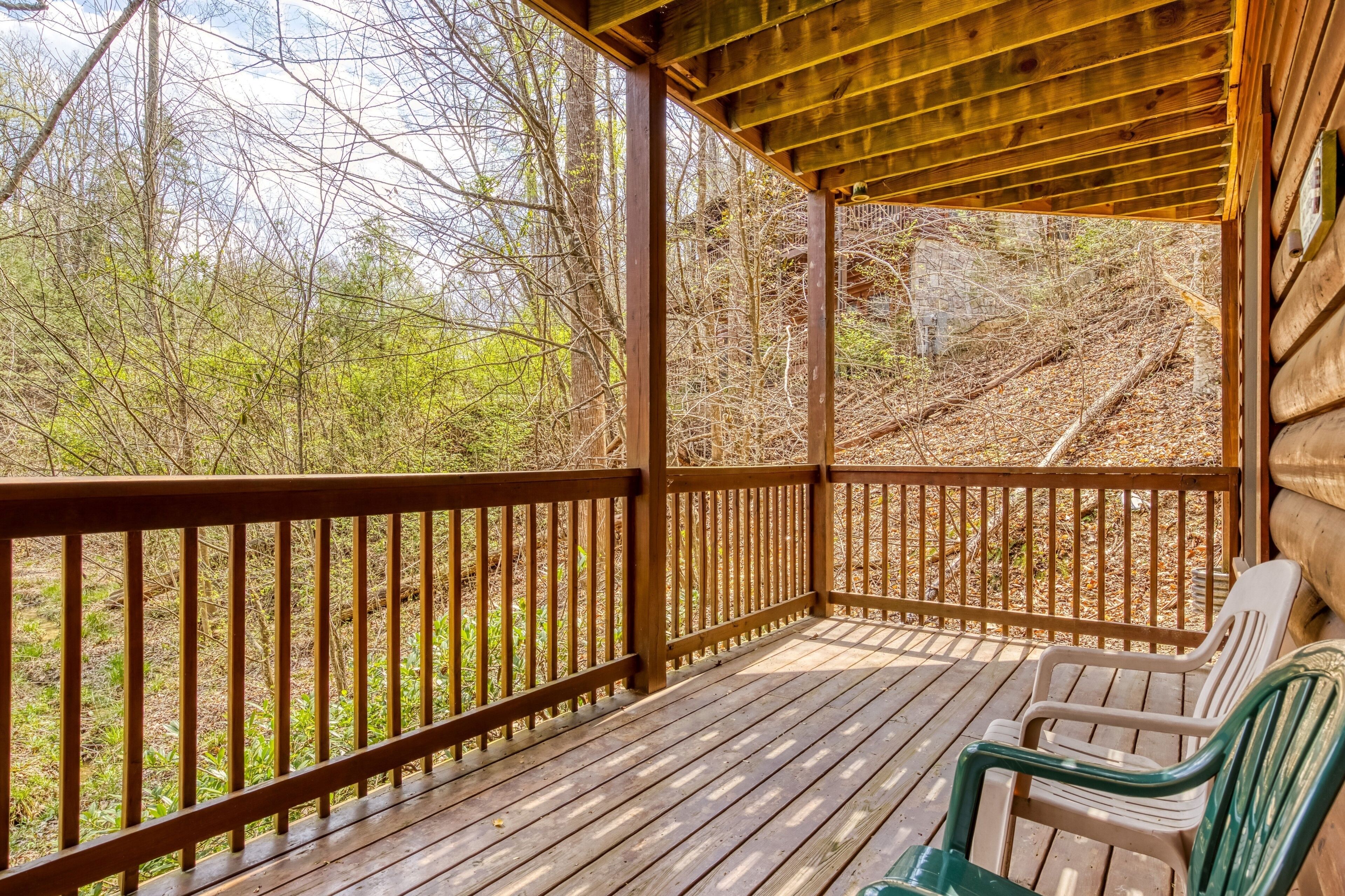 A wooden deck with railings, a bench, and a view of a forested area.