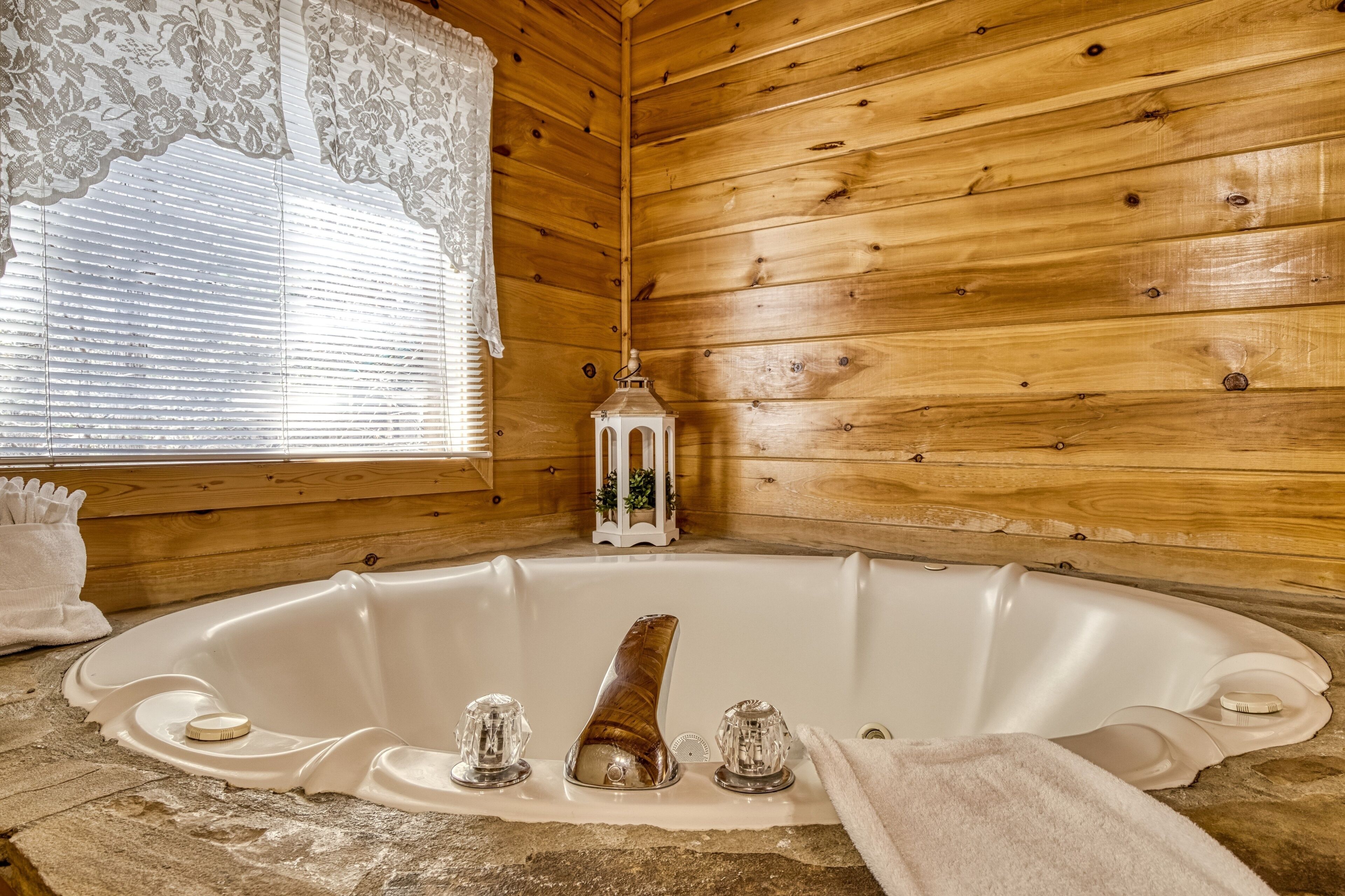 Eine Holzhütte mit einer großen Badewanne, Spitzenvorhängen und einer Laterne.