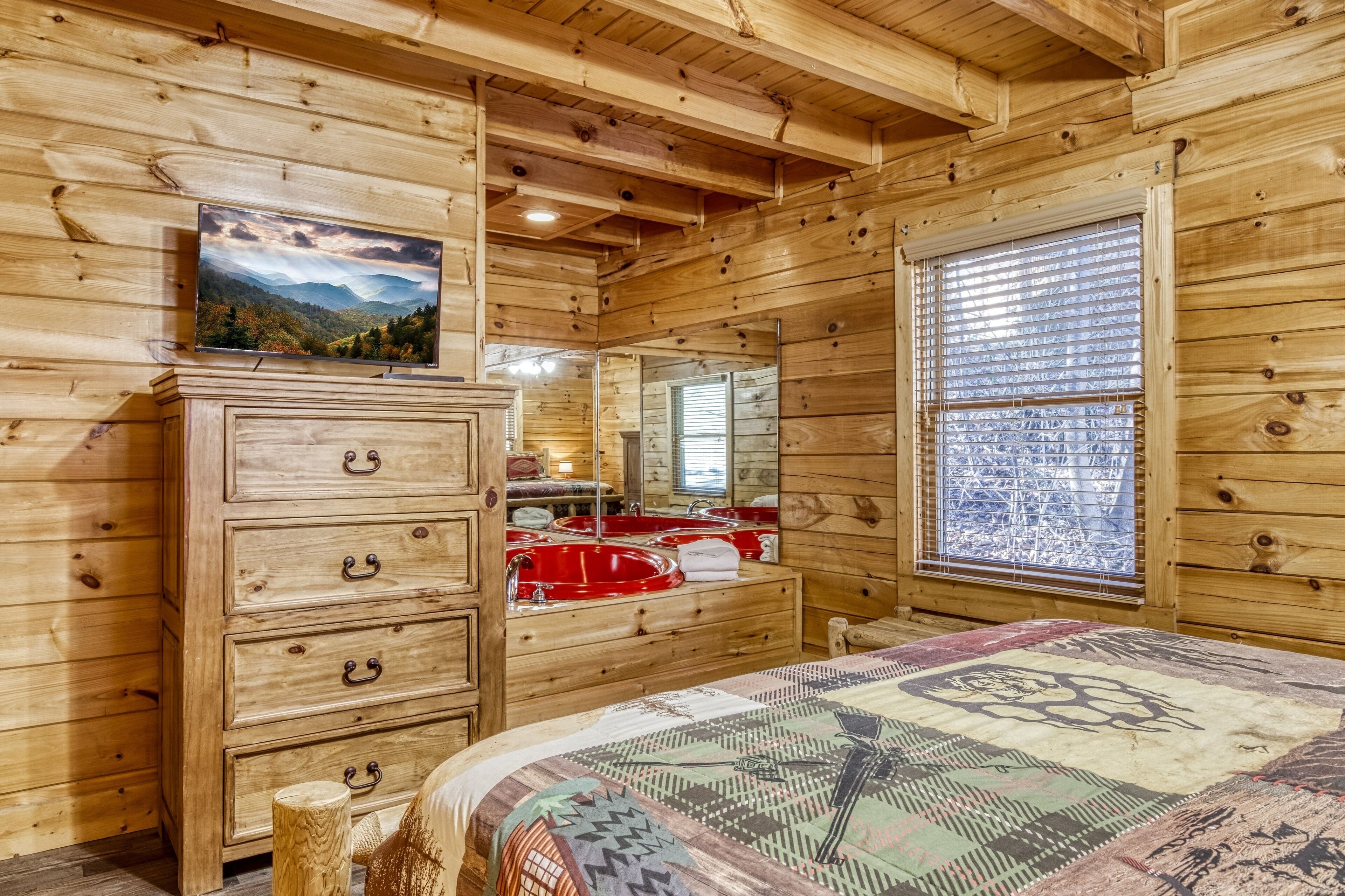 A wooden cabin room with a bed, a dresser, a mirror, and a window with blinds.