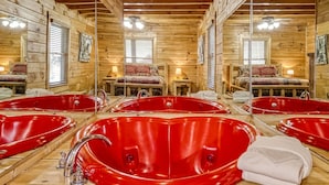 Una cabaña de madera con un espejo grande que refleja una bañera roja y una cama con una manta roja.