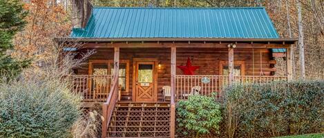 Une cabane rustique avec un toit en métal vert, une véranda en bois et une décoration en forme d’étoile rouge.