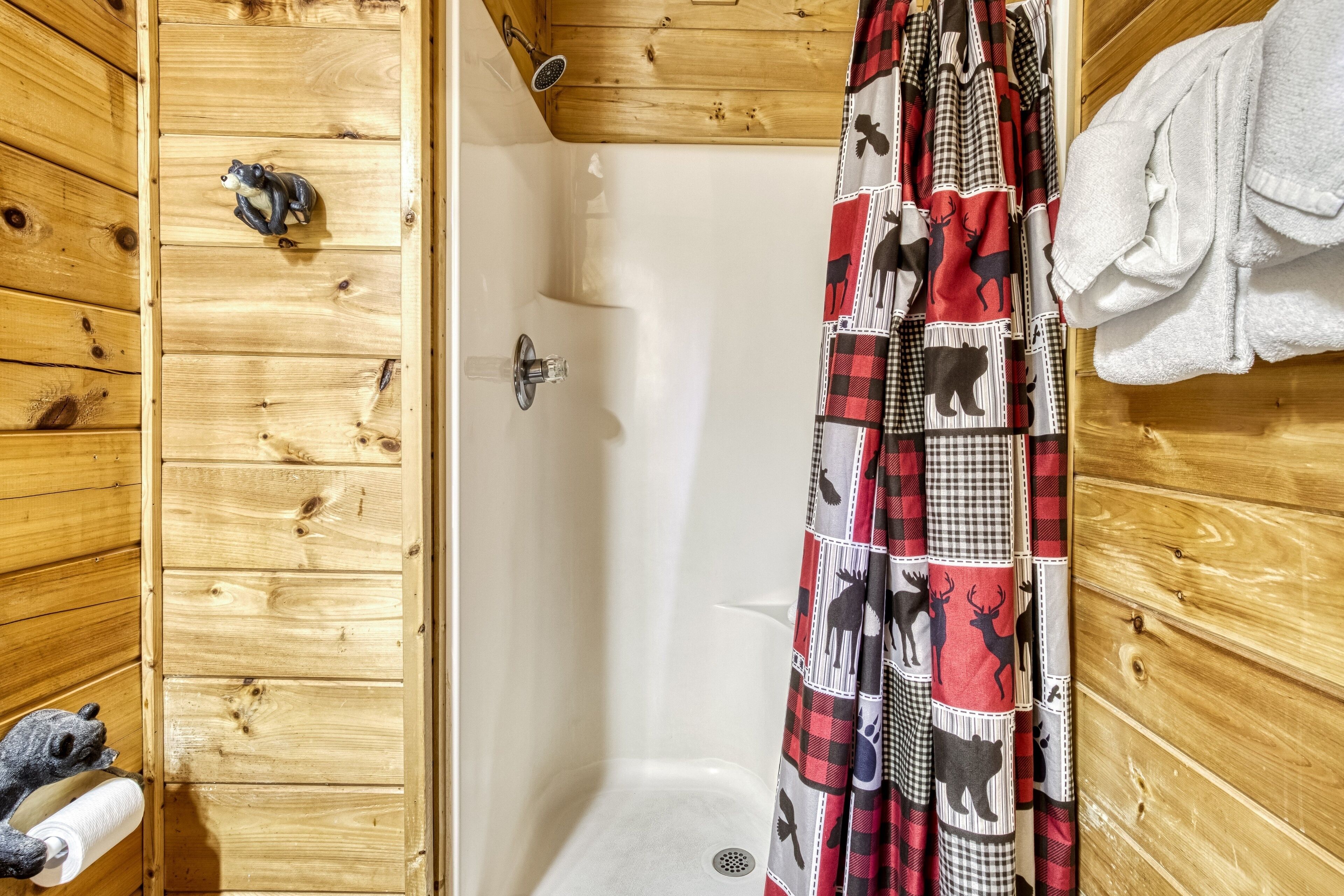 A wooden cabin bathroom with a shower curtain featuring animal prints, a towel rack, and a small rug.