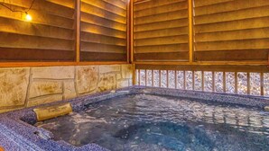 Un jacuzzi con pared de piedra y techo de madera, rodeado por una terraza de madera.