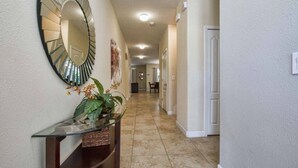 A hallway with a round mirror, a glass console table with a plant, and a tiled floor. - Paradise Palms-6 bedrooms House w-pool-3509PP 6 Home by RedAwning (Kissimmee)