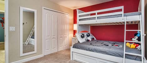 Une chambre avec un lit superposé, une armoire, un miroir et une échelle.