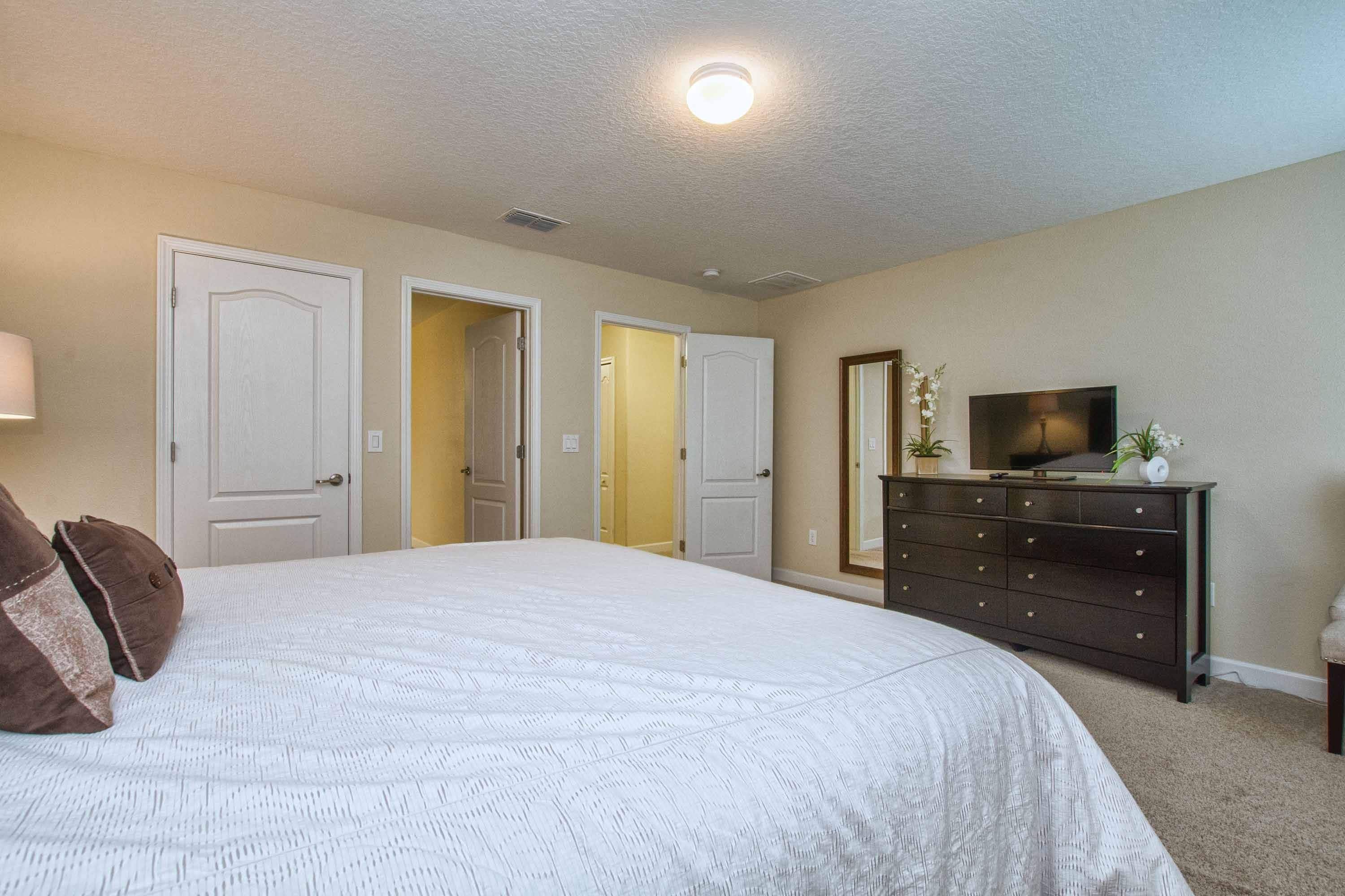 A bedroom with a large bed, a dresser, a television, and two doors leading to other rooms.