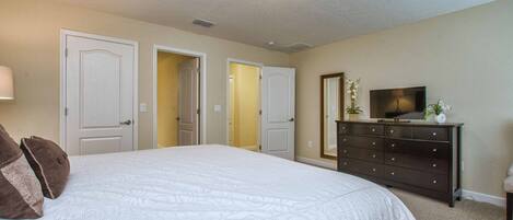 A bedroom with a large bed, a dresser, a television, and two doors leading to other rooms.