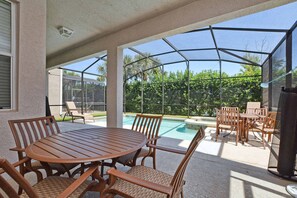 Pátio externo com piscina, área de estar coberta e mesa com cadeiras.