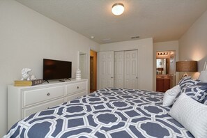 Ein Schlafzimmer mit Bett, Kommode, Fernseher und einer Tür zu einem anderen Raum.