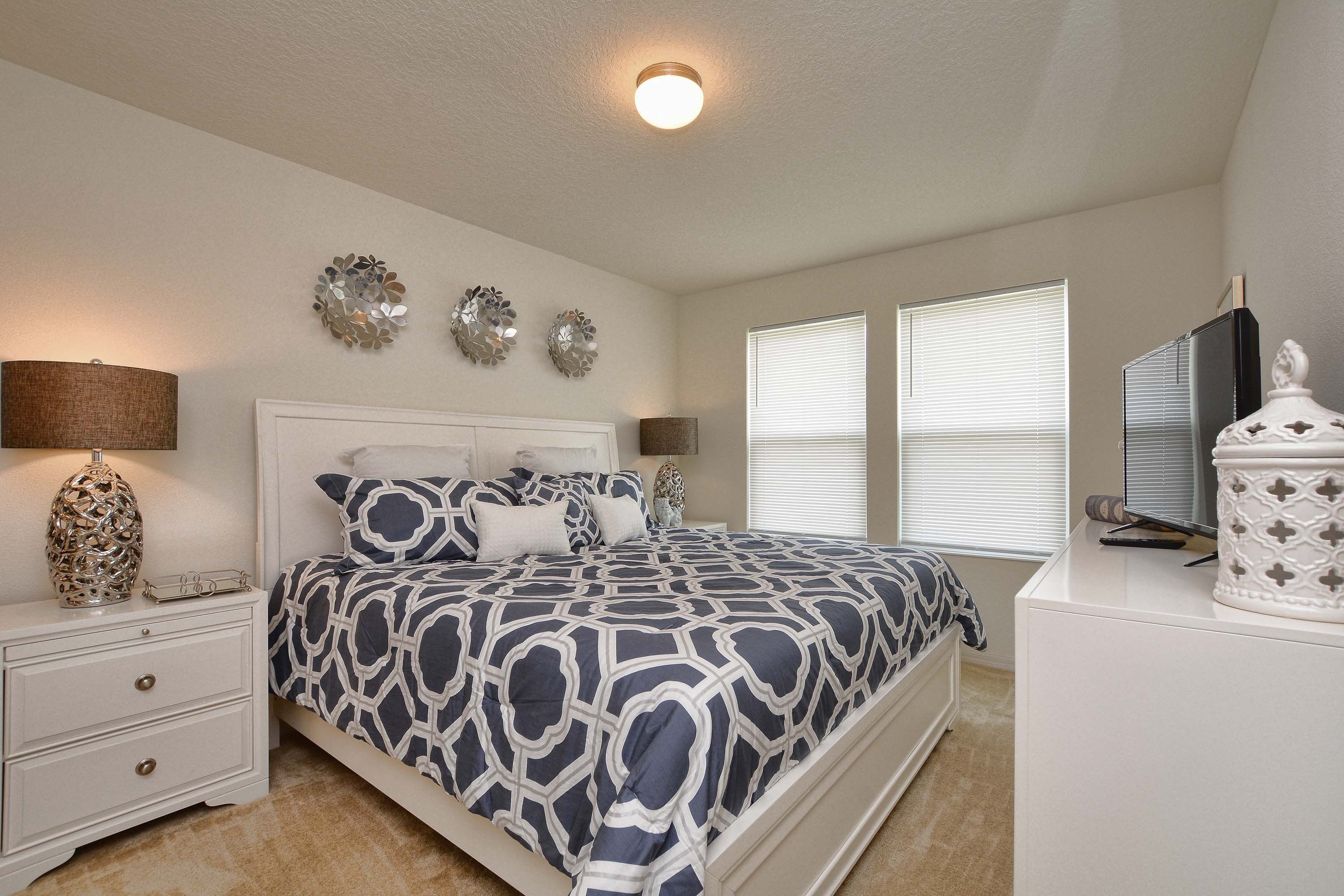 A bedroom with a bed, bedside tables, wall art, and a television.