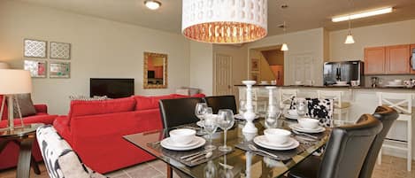 Comedor con una mesa de vidrio dispuesta para seis personas, rodeado de sofás rojos y un tapete con estampado en blanco y negro.