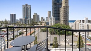 A balcony with a table and chairs overlooking a cityscape with tall buildings and a parking lot. - Surfers Paradise Beach & Ocean View Unit (Level 7) (Surfers Paradise)