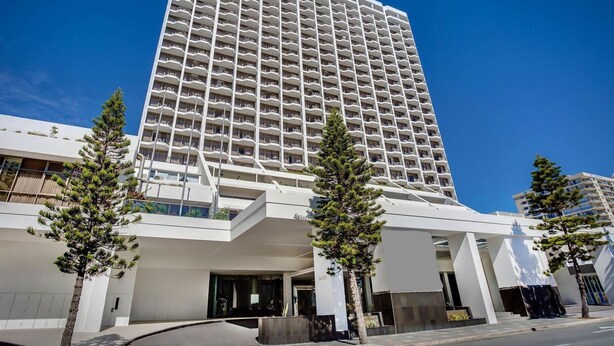 A modern high-rise hotel with a prominent entrance, multiple balconies, and a clear sky. - Surfers Paradise Beach & Ocean View Unit (Level 7) (Surfers Paradise)