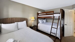 A hotel room with a bunk bed, a single bed, a bedside lamp, and a door. - 111 El Matador 2 Bedroom Condo by RedAwning (Fort Walton Beach)