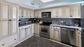 A modern kitchen with light-colored cabinetry, a black tiled backsplash, stainless steel appliances, and a skylight. - 111 El Matador 2 Bedroom Condo by RedAwning (Fort Walton Beach)