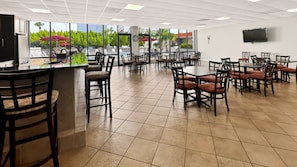 A spacious indoor area with multiple tables and chairs, a bar area, and large windows offering views of an outdoor pool and greenery. - 111 El Matador 2 Bedroom Condo by RedAwning (Fort Walton Beach)