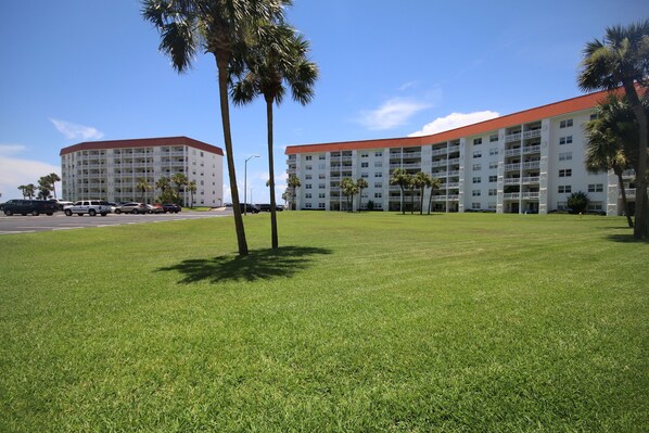 A hotel with a red roof and multiple balconies, surrounded by a well-maintained lawn and palm trees. - 111 El Matador 2 Bedroom Condo by RedAwning (Fort Walton Beach)