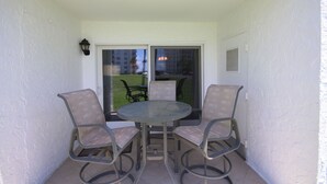 A small balcony with a glass door leading to a patio area. There are two metal chairs and a round table. - 111 El Matador 2 Bedroom Condo by RedAwning (Fort Walton Beach)