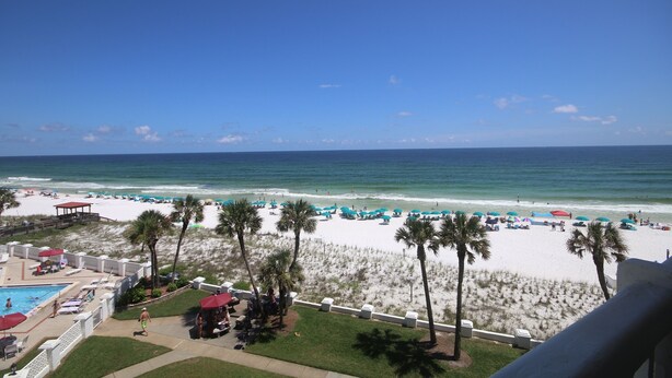 A beach view with a pool area, palm trees, and beach umbrellas.