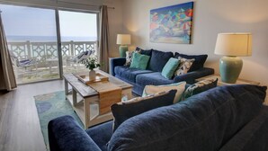 A living room with a sofa, two lamps, a painting, and a view of the sea through a balcony.