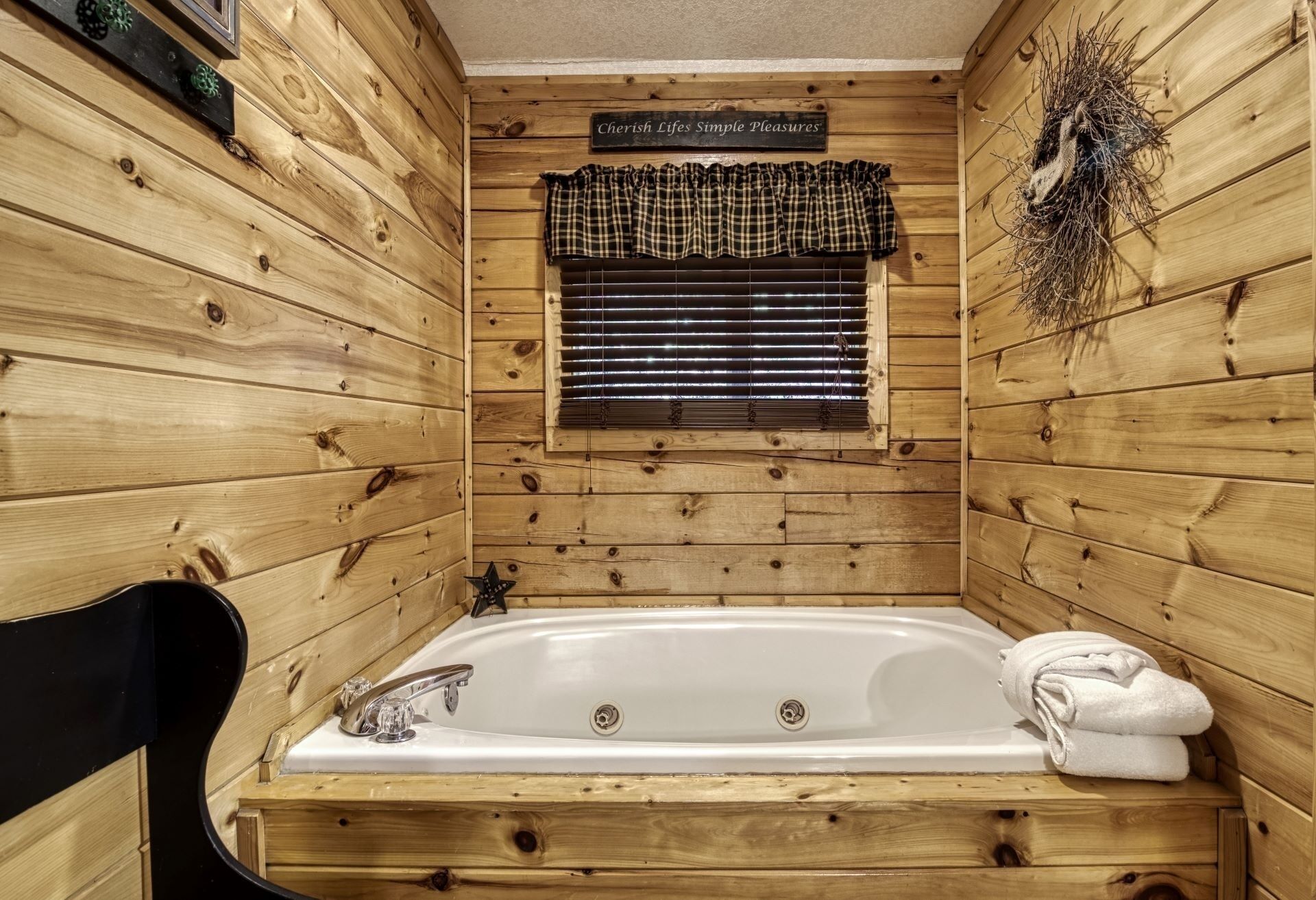Interieur van een houten hutje met een wit bad, een ruit gordijn met ruitpatroon, en een bordje met de tekst 'Cherish Lifestyles Simple Pleasures'.