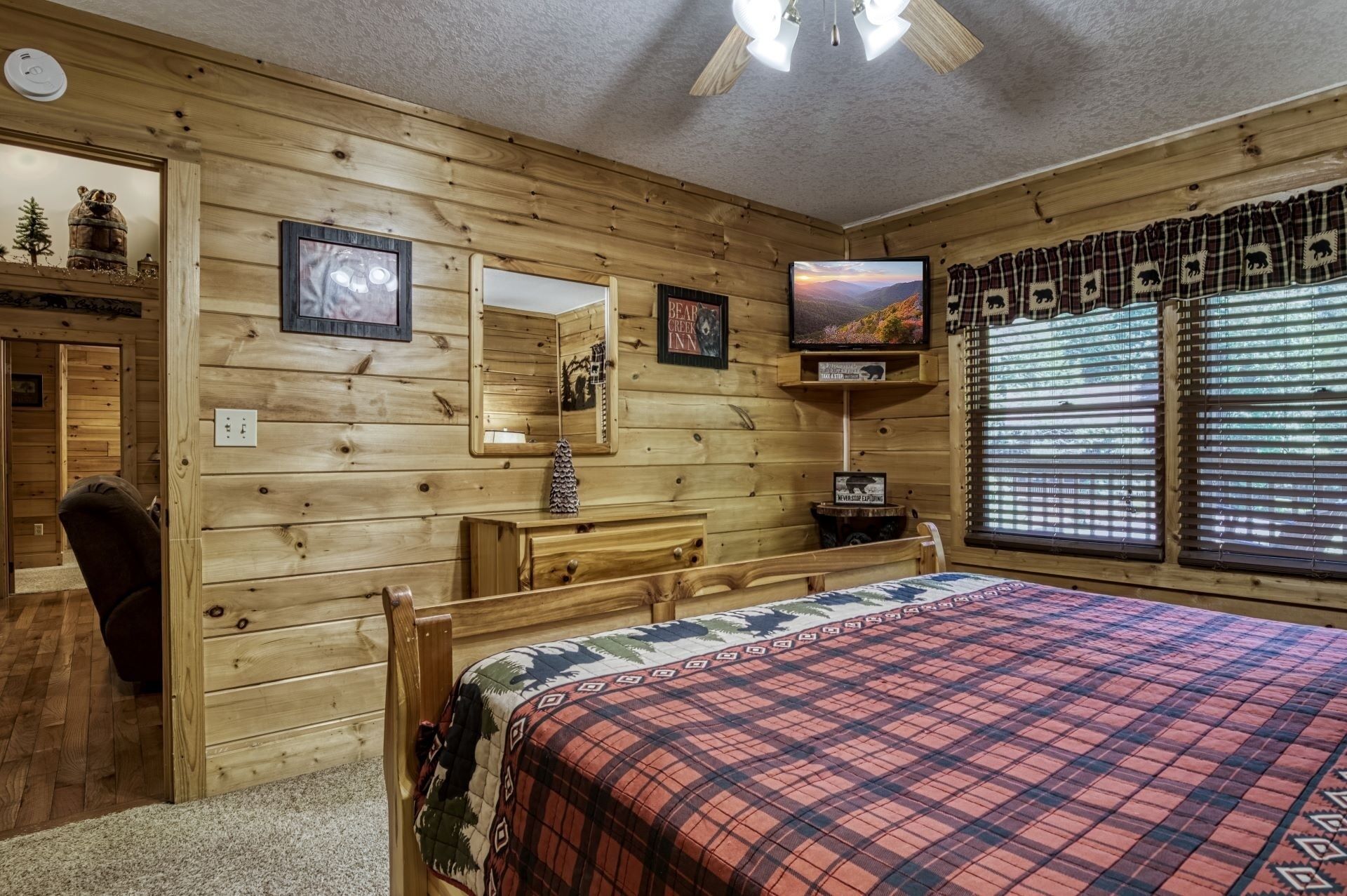 A wooden cabin room with a bed, a dresser, a mirror, and a window with blinds.