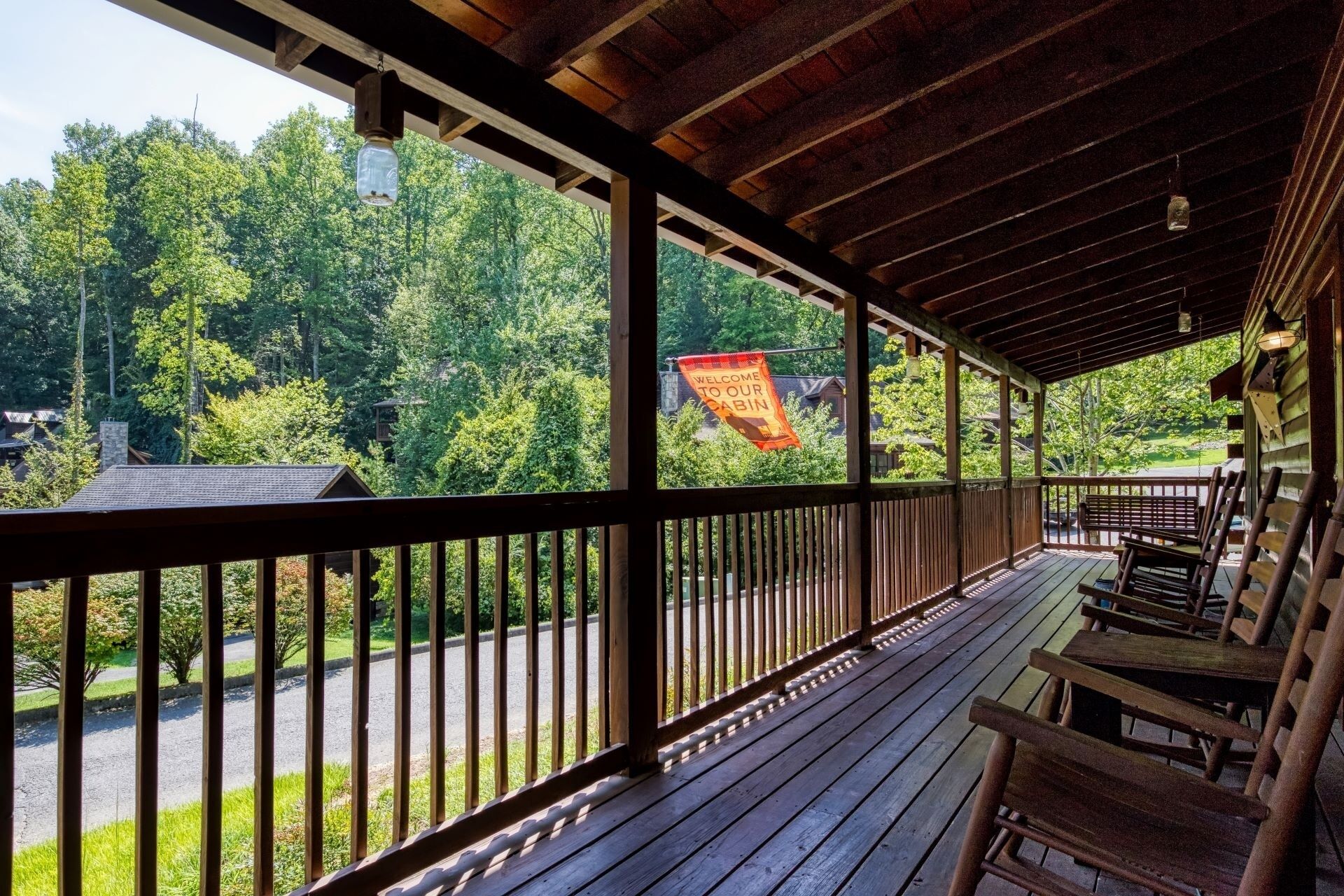 A wooden deck with a view of a forested area and a 'Welcome to Our Cabin' sign.