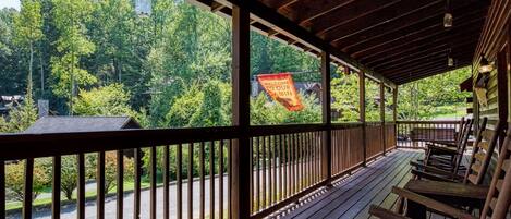 A wooden deck with a view of a forested area and a 'Welcome to Our Cabin' sign.