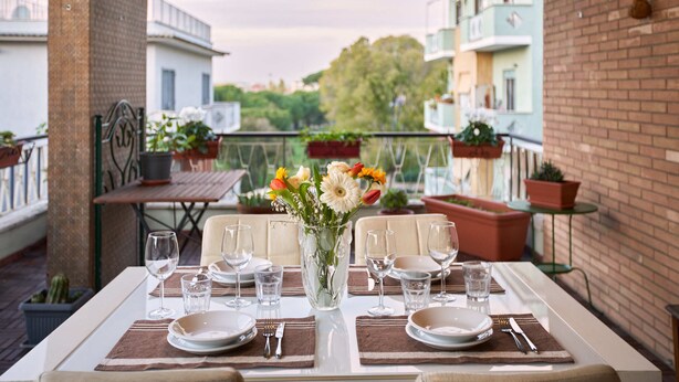 A dining table set with plates, glasses, and cutlery, surrounded by potted plants and a vase of flowers. - Luxurious Terrace and confort close Rome Center (Roma)