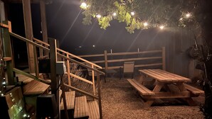 A wooden deck with a picnic table and benches, surrounded by a wooden fence and string lights.