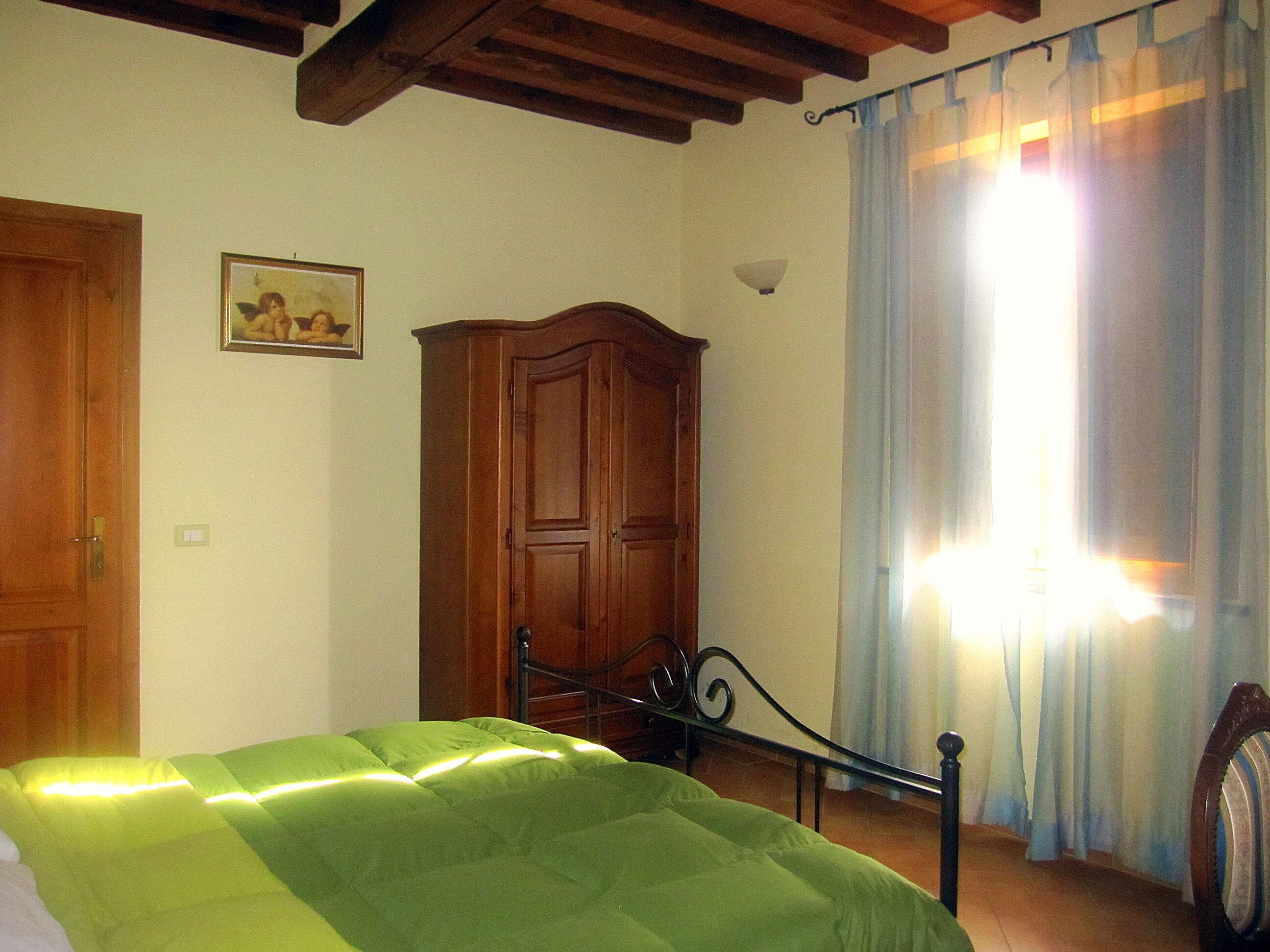 A bedroom with a bed, wooden wardrobe, and a window with curtains.