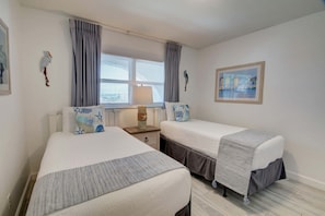 A hotel room with two beds, a window with curtains, a nightstand with a lamp, and a painting on the wall. - 363 El Matador 2 Bedroom Condo by RedAwning (Fort Walton Beach)