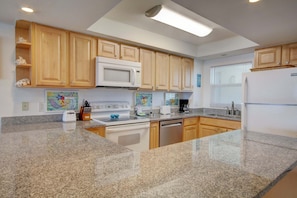 A kitchen with granite countertops, wooden cabinets, a microwave, a stove, a dishwasher, and a refrigerator. - 363 El Matador 2 Bedroom Condo by RedAwning (Fort Walton Beach)