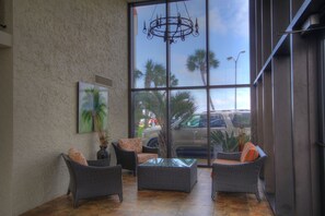 Relax in a spacious area with a high ceiling, large windows, and a view of palm trees and parked cars outside.