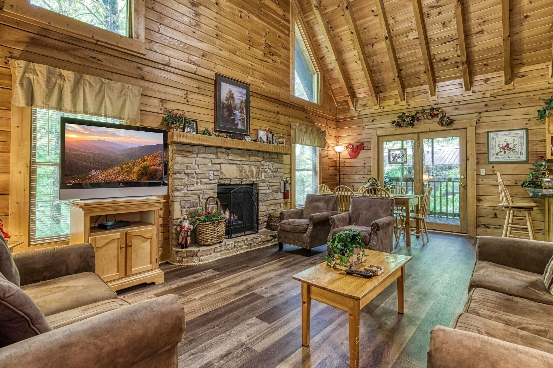 A cozy cabin interior with a stone fireplace, wooden walls, and a large TV.