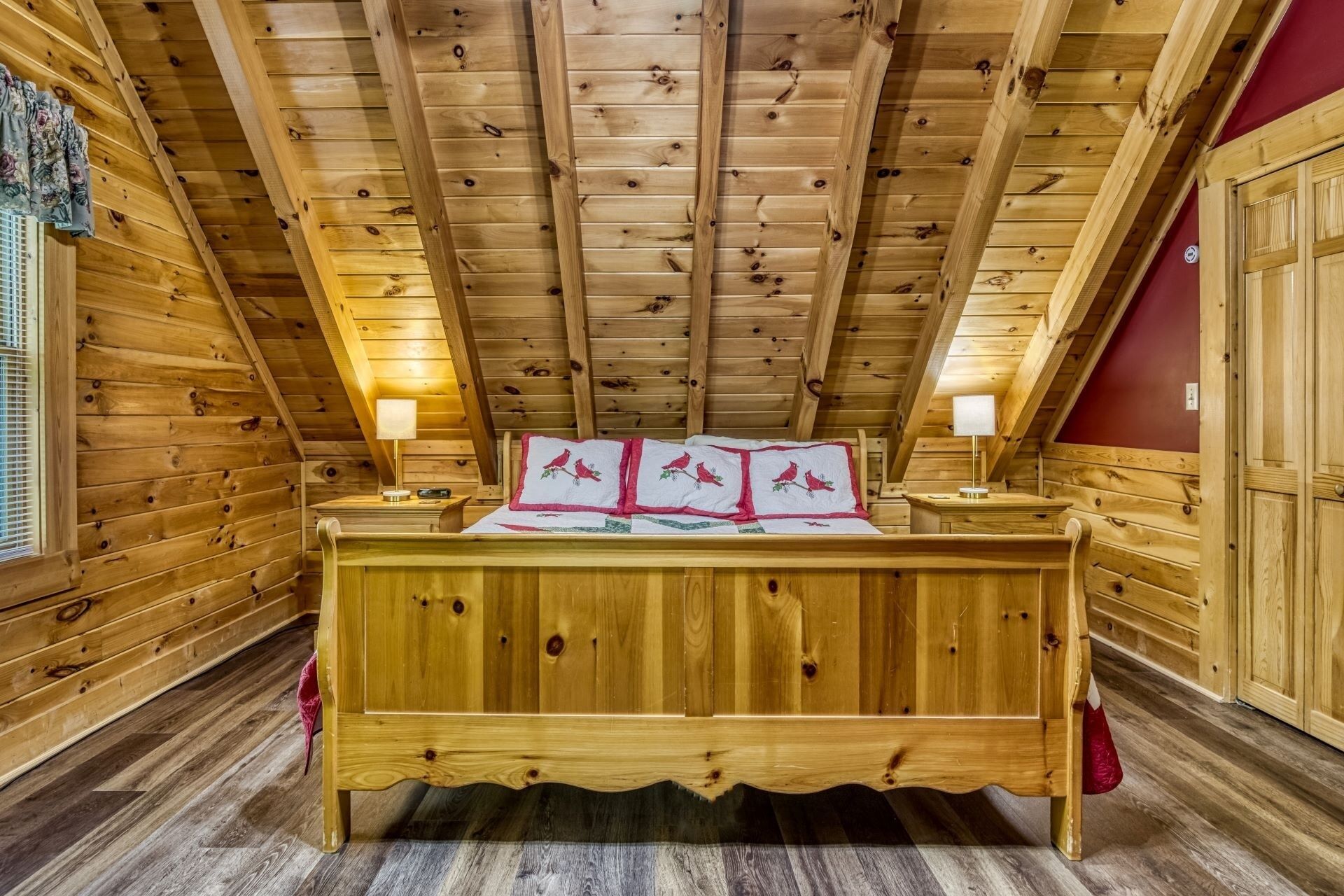Une chambre dans un chalet en bois, avec un lit, deux lampes de chevet et un mur rouge.