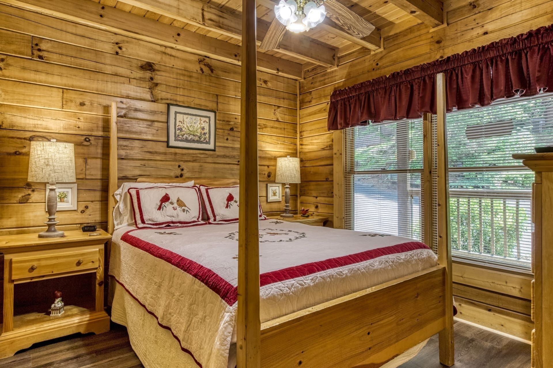 A wooden cabin bedroom with a four-poster bed, two bedside tables, and a large window with blinds.