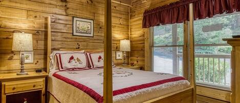 A wooden cabin bedroom with a four-poster bed, two bedside tables, and a large window with blinds.