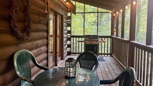 A wooden cabin with a covered porch, a grill, and a table with chairs. - Er215 - Red Bird Haven Great Location - Close To Town! 3 Bedroom Cabin by RedAwning (Pigeon Forge)