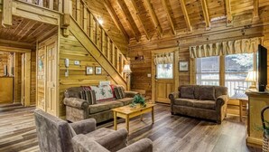 A cozy log cabin interior with a staircase, two sofas, a coffee table, and a TV. - Er215 - Red Bird Haven Great Location - Close To Town! 3 Bedroom Cabin by RedAwning (Pigeon Forge)