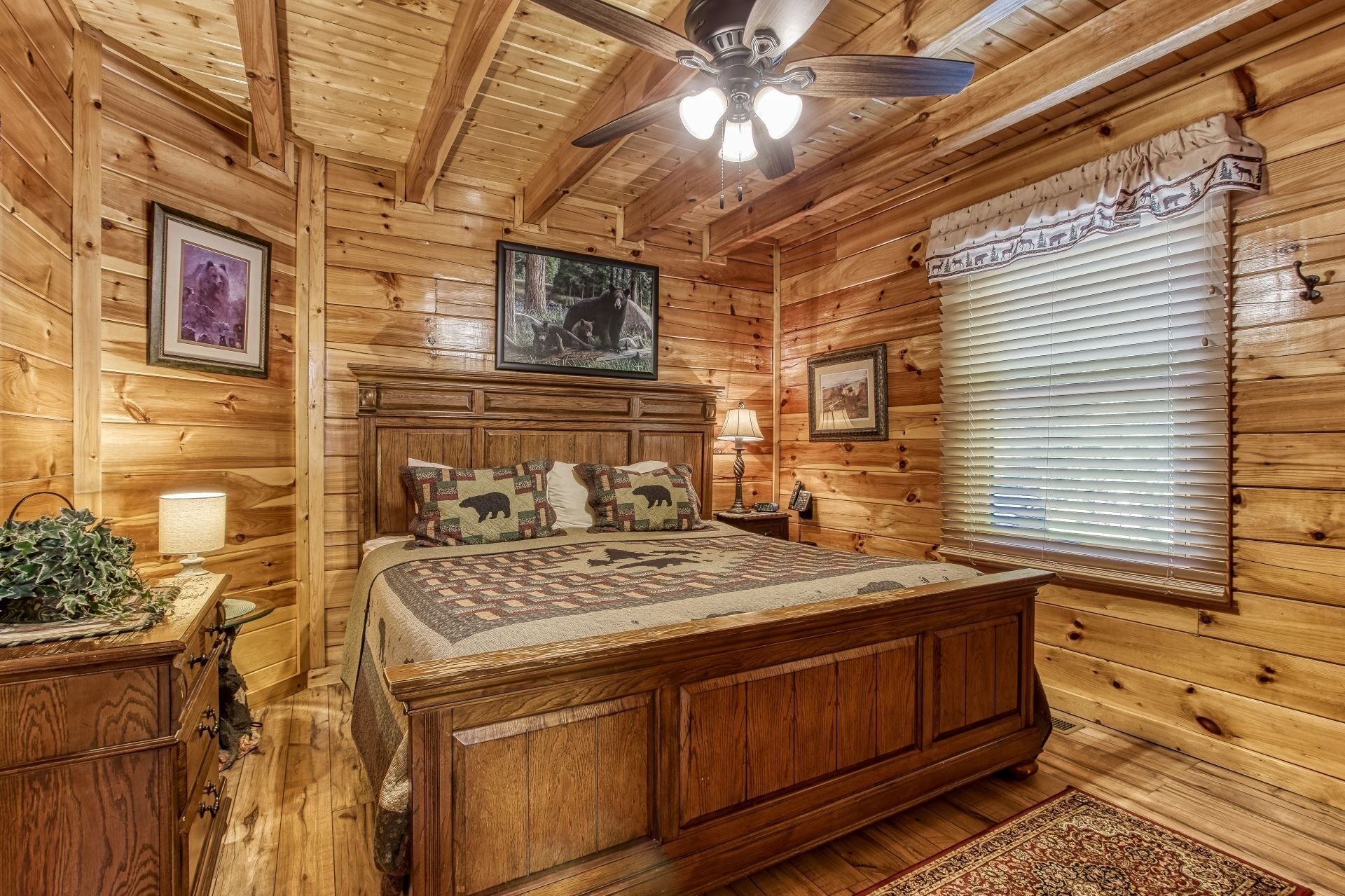 Une chambre dans une cabane en bois, avec un lit, un ventilateur de plafond et des tableaux encadrés accrochés aux murs.
