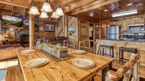 A wooden interior with a dining table set for four, a fireplace, and a kitchen area. - Majestic Mountain View - Great Location! - Convenient To Everything! 2 Bedroom Cabin by RedAwning (Pigeon Forge)