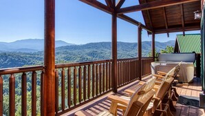 A wooden deck with a view of mountains. There are wooden chairs and a table. - Majestic Mountain View - Great Location! - Convenient To Everything! 2 Bedroom Cabin by RedAwning (Pigeon Forge)