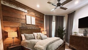 Una camera da letto con una testiera in legno, un letto con molti cuscini, un comodino con una lampada, una cassettiera e una ventola a soffitto.