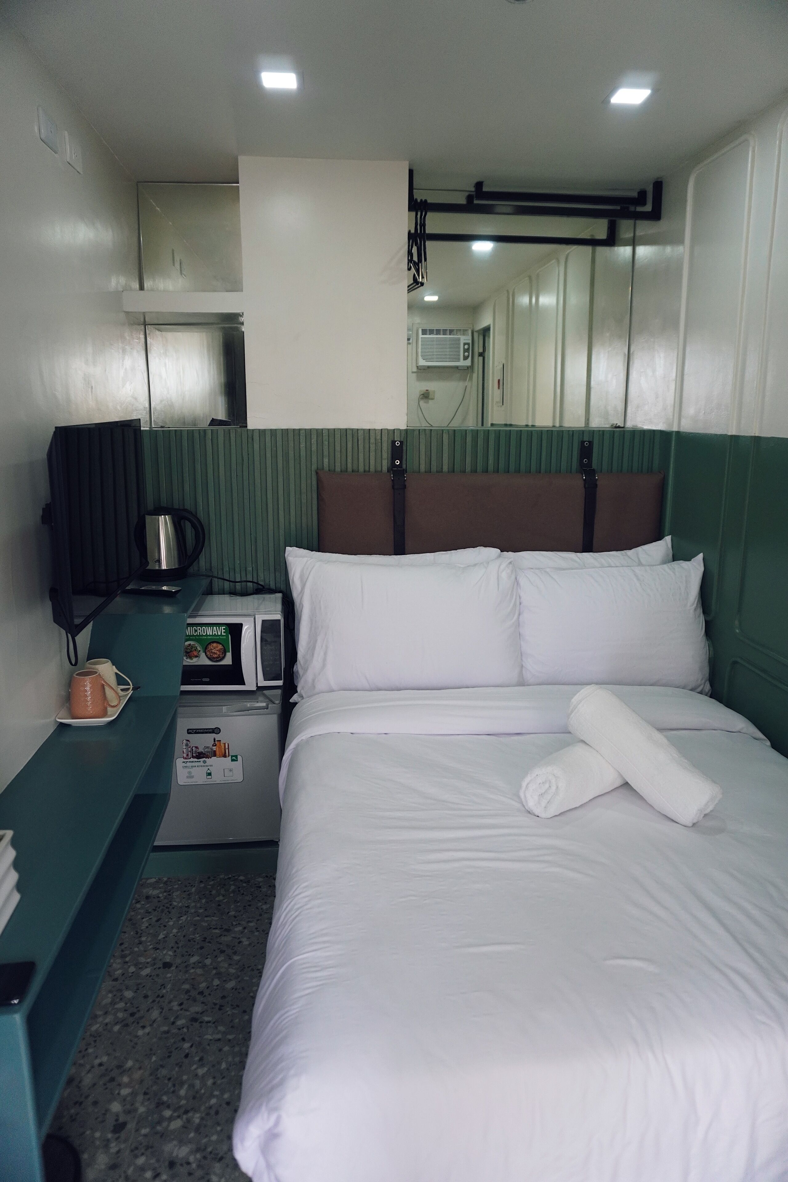 A hotel room with a bed, a microwave, a coffee maker, a telephone, and a small table with a cup.