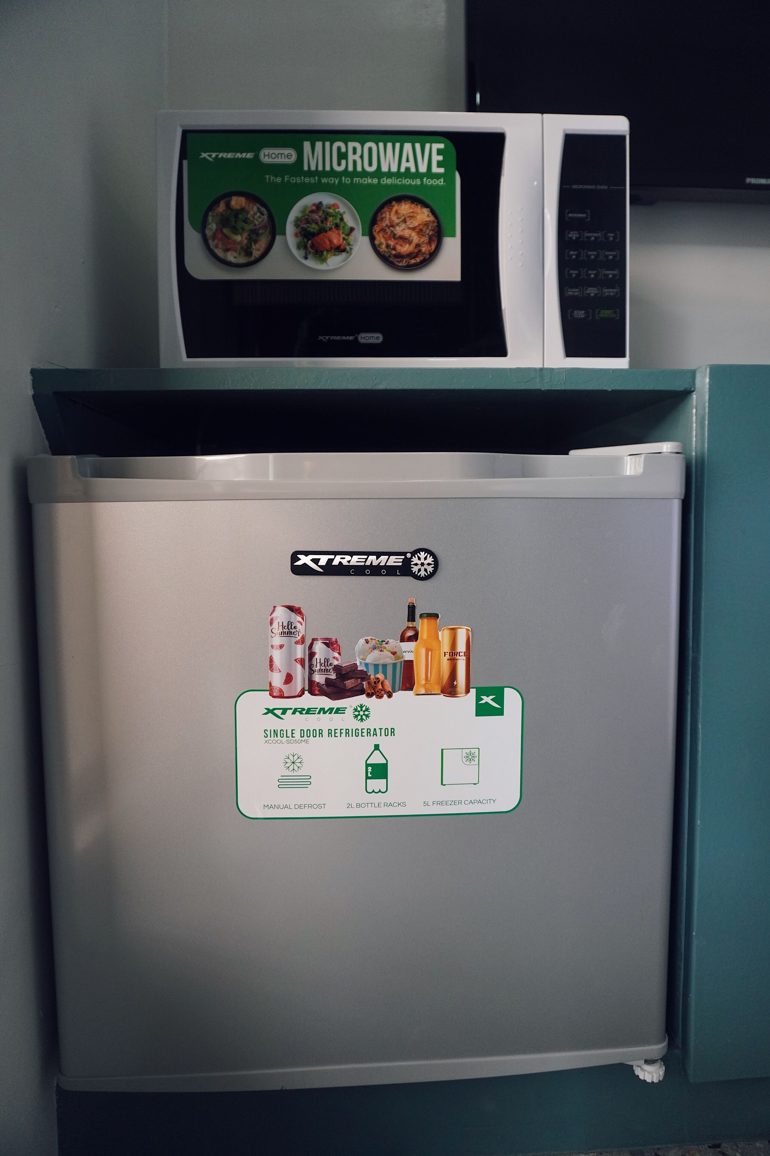 Un refrigerador con microondas encima, etiquetado como refrigerador de una puerta con descongelación manual, 2 parrillas para botellas y capacidad de congelador.