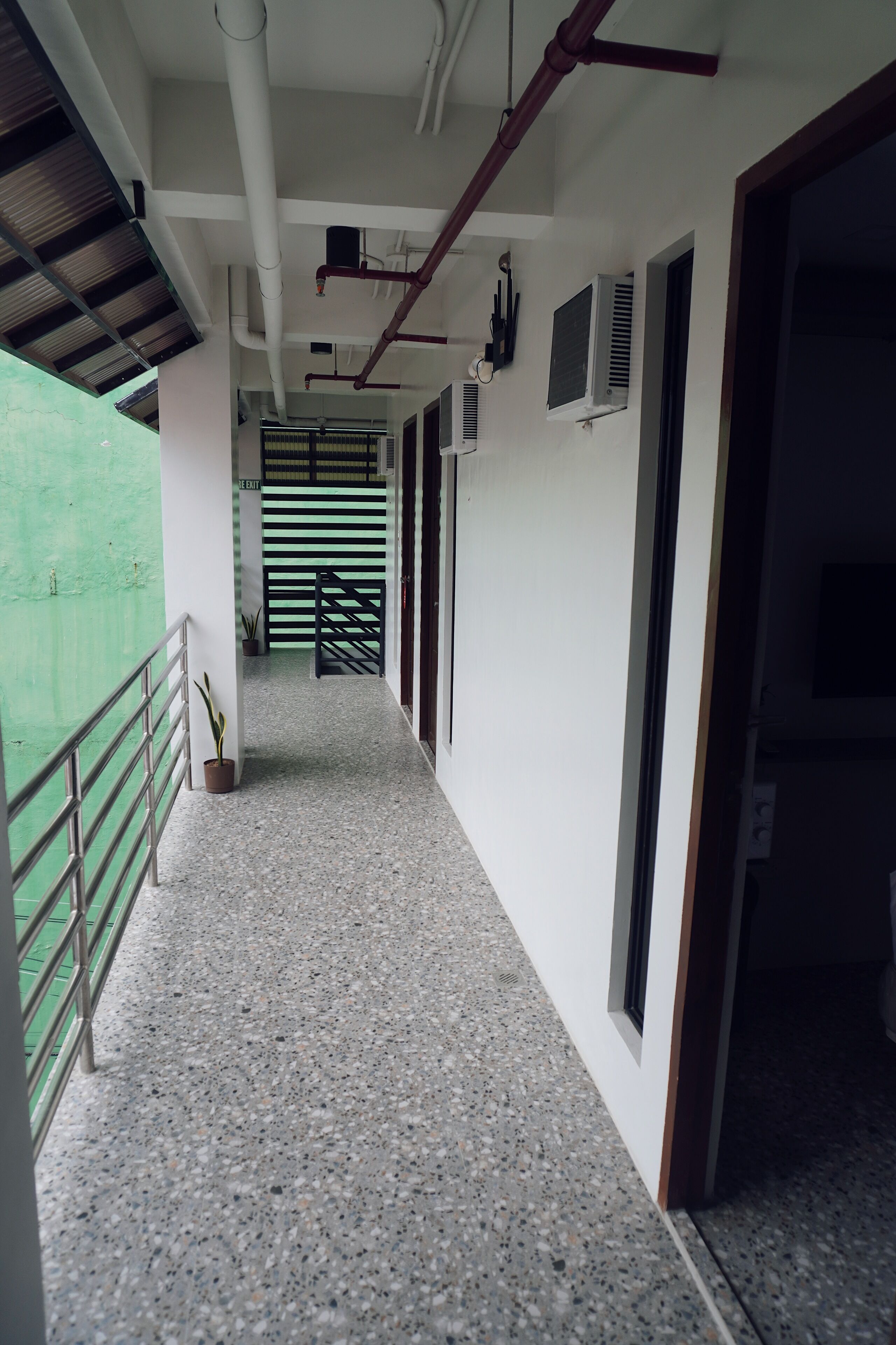 A corridor with a metal railing, a potted plant, and a door leading to a room.