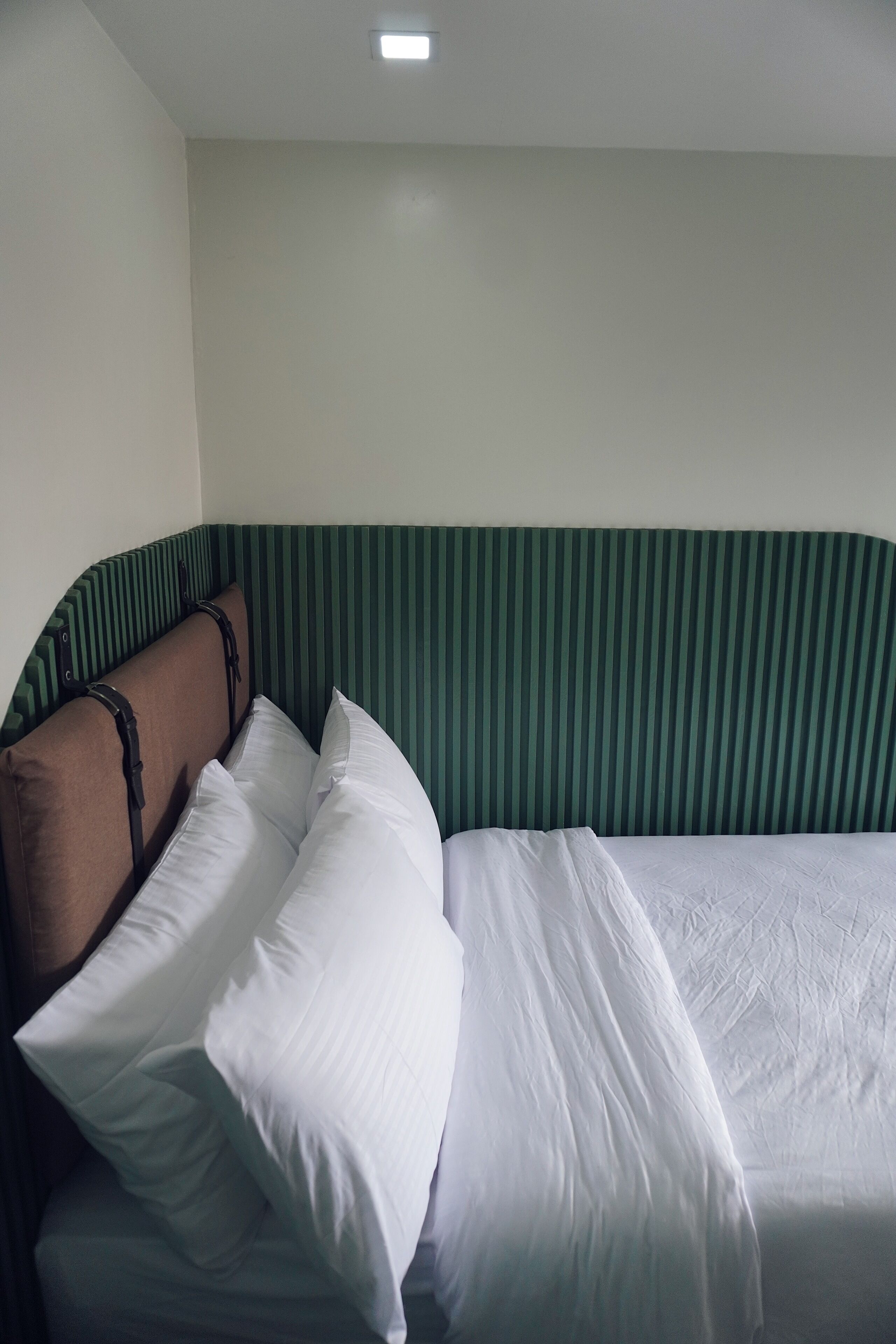 Una cama con cabecera verde a rayas, ropa de cama blanca y dos almohadas.