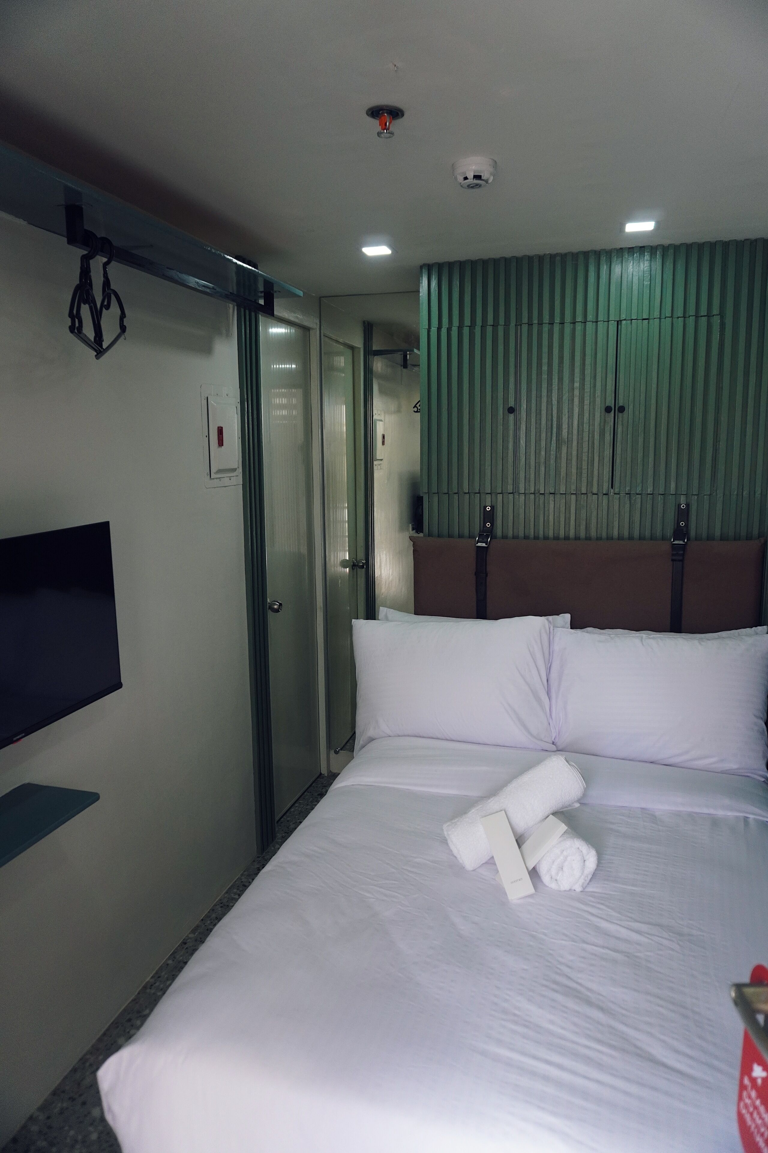 Habitación de hotel con una cama, un televisor montado en la pared, una puerta de cristal y un panel verde en la pared.